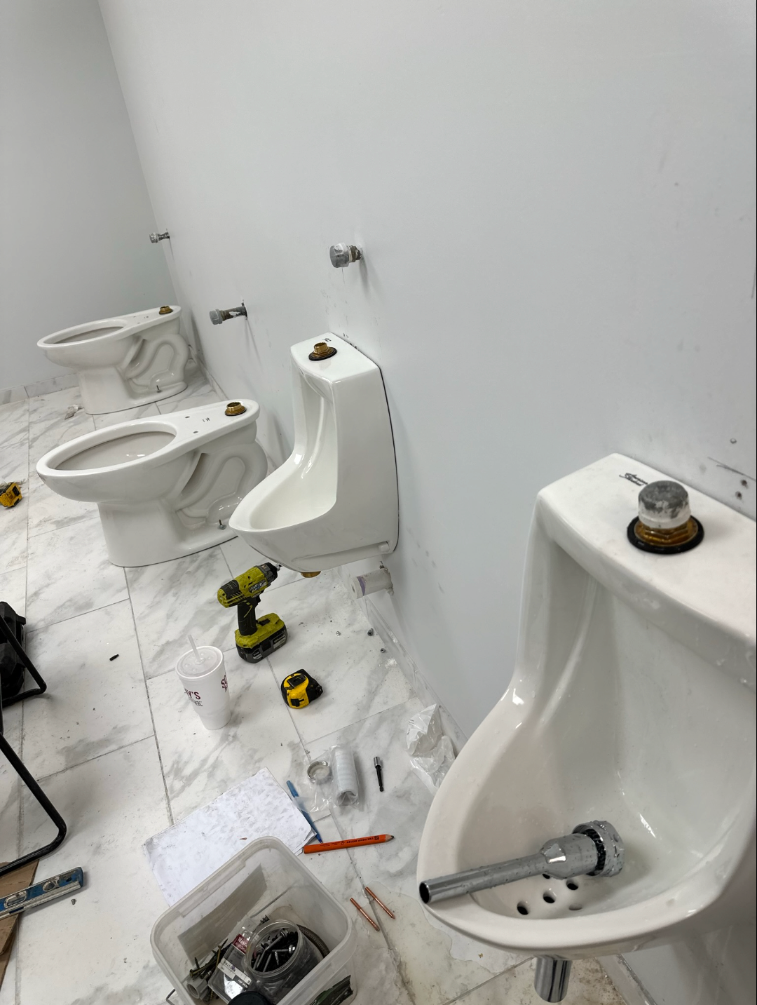 Commercial restroom mid-install with new toilets and urinals set on tile floor