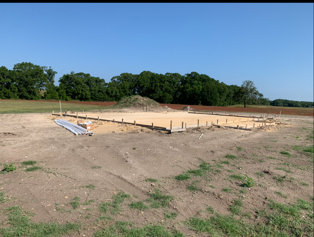 Foundation pad prepped with plumbing stub-ups and PVC pipe on rural build site
