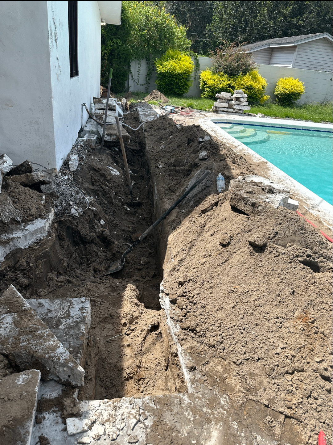 Trench excavated along a stucco home next to a pool for plumbing line work