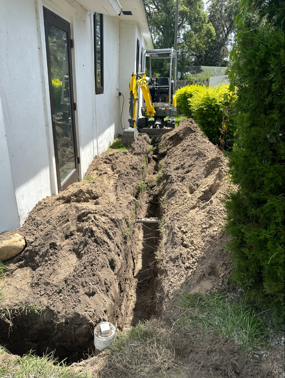 Long exterior trench dug along a home for sewer line replacement with mini excavator